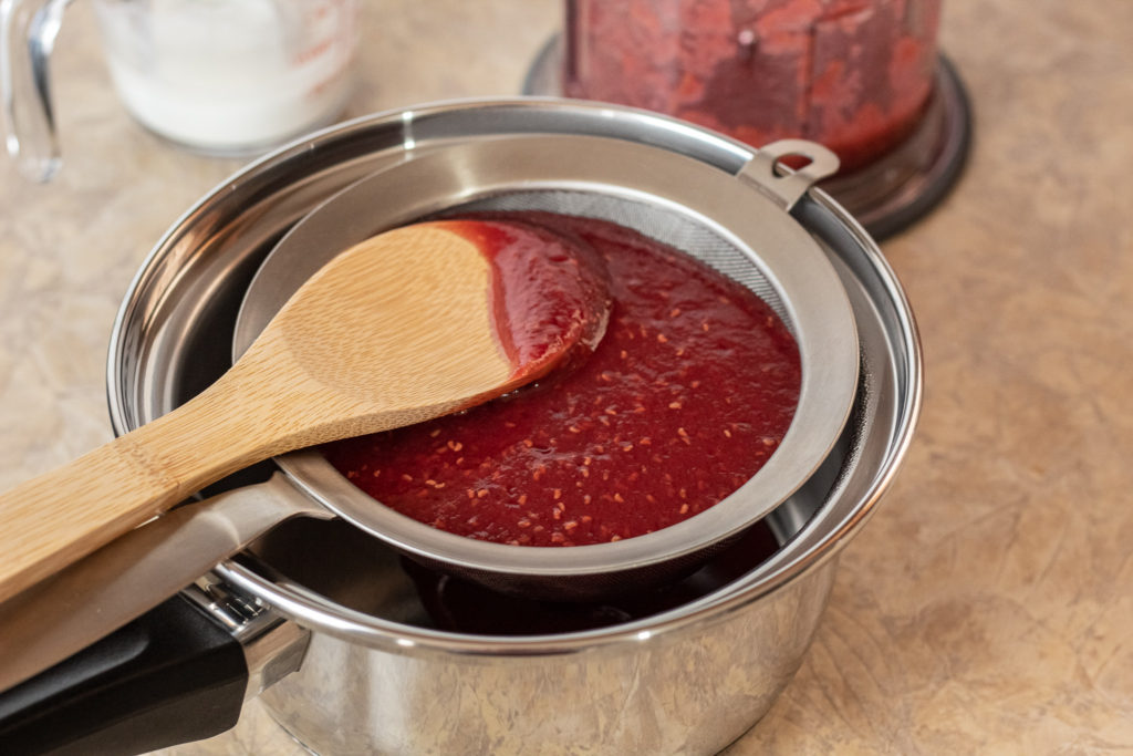 Straining raspberry filling into a clean saucepan.